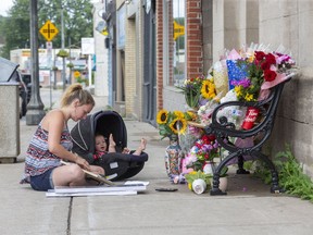 With seven-month-old daughter Abigail at her side, Destiny Fick fills a frame with photos of her cousin Ashten Elizabeth Fick before adding it to a memorial for the mother of three on Thames Street  in Ingersoll on Sunday. Ashton was struck and killed  by a transport truck as she crossed the street on Friday. Derek Ruttan/The London Free Press/Postmedia Network