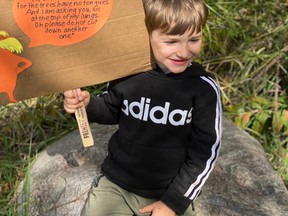 A young boy holds up a sign in protest of the removal of the “Zombie Forest” in the Town of Gibbons. Photo Supplied.