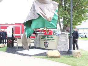 The Stony Plain Fire Department uses their truck's crane ladder to lift the veil on the new memorial bench space outside the station in the community Sunday. It will have the names of former firefighters who have passed on engraved on it in the future.