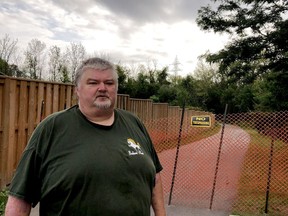 Marco Malovic stands by the fence he erected on Aspen Drive Wednesday morning, blocking access to the Brock Trail over a property dispute. (RONALD ZAJAC/The Recorder and Times)