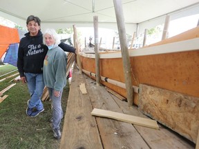 Chuck Commanda, Algonquin knowledge keeper, and Mary Farrar, from Friends of Kingston Inner Harbour, stand next a birch bark canoe on Saturday. The canoe is being hand built in the coming weeks in Douglas R. Fluhrer Park. (Meghan Balogh/The Whig-Standard)