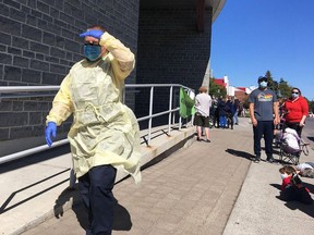 A health-care worker strides past long lines of people waiting to be tested for COVID-19 at the Leon's Centre assessment centre on Monday. (Elliot Ferguson/The Whig-Standard)