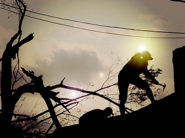 Silhouetted against the sun, two people work to quickly patch up a roof following a severe storm, likely a microburst, that blew through the Drive-In Road area of Laurentian Valley, just east of Pembroke, on Sunday afternoon, Sept. 13. Anthony Dixon