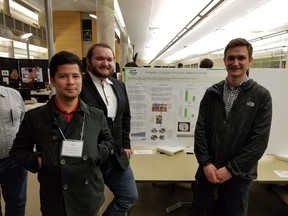 Ralph Dabao (from left to right), Austin Bruder, and Nathan McMurray stand as a group with a presentation showing the details of their lacrosse stick optimization.
