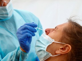 A nurse wearing a protective suit and a face mask uses a nose swab on a patient in a testing area outside a hospital amid the coronavirus disease (COVID-19) outbreak in Brussels