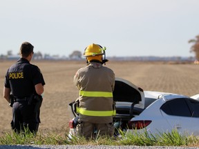 A Lambton OPP officer and an Enniskillen and Oil Springs firefighter watch police drive into a field near the site of a single-car crash on Saturday October 17, 2020 in Enniskillen Township, Ont. Terry Bridge/Sarnia Observer/Postmedia Network