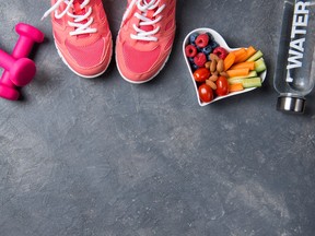 Fitness concept, pink sneakers, dumbbells, bottle of water and heart shaped plate with vegetables and berries on a grey background, top view, healthy lifestyle