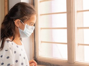 A sad girl looks out the window during home isolation in the COVID-19 pandemic.