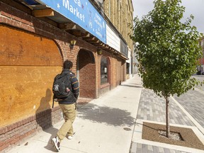 A person walks down Talbot Street in St. Thomas past a boarded-up flea market that has signs for needle exchange posted on the few remaining windows. Local businesses are demanding action from the city to address loitering and littering concerns that have increased since a drop-in shelter opened. (Mike Hensen/Postmedia Network)