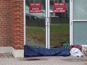 A person rests on the ground in front of doors at the Sudbury Community Arena in Sudbury, Ont. on Wednesday October 21, 2020.