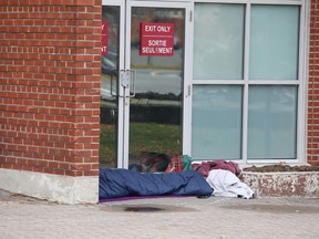 A person rests on the ground in front of doors at the Sudbury Community Arena in Sudbury, Ont. on Wednesday October 21, 2020.