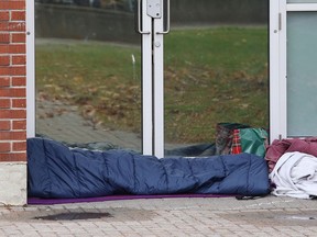 A person rests on the ground in front of doors at the Sudbury Community Arena in Sudbury, Ont. on Wednesday October 21, 2020.