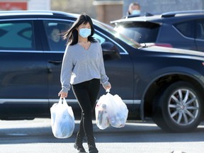 A woman wearing a mask carries groceries in a Pembina Highway parking lot in Winnipeg on Monday.