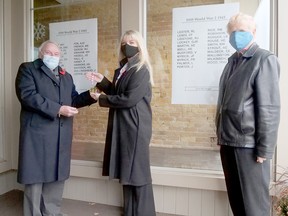 Les Burden, president of the Tillsonburg Military History Club, on the left, presents a Local Hero award to Carrianne Hall, owner of Trinkets Gift Shoppe. Tillsonburg Military History Club member Frank Moore, on the right, stands next to the display's list of local soldiers who died in the Second World War. (Chris Abbott/Norfolk and Tillsonburg News)