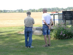 Looking west over a Field of Dreams, Manley Fraleigh (left) and Don Benedict reminisce about days gone by. In the middle ground, the just-harvested wheat field that used to be Benedict's SnyeView Orchards. At the right of the photo are the steps to Whitebread United Church and the historical marker that marks where it once stood. John Martinello photo