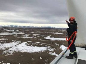 A wind turbine technician stands at the top of a southern Alberta turbine.