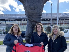 Brantford Girls Hockey Association registrar Cathy Drinkwater (left) holds an Ice Cats jersey outside the Wayne Gretzky Sports Centre, along with Lexi Cross  and her mother, Leslie Cross. The BGHA has initiated three annual scholarships for its players, including one named in honour of longtime coach Brian Cross, who died Oct. 16. He is Lexi's father and Leslie's husband.