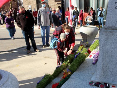 Three-year-old Cullen Cameron and joined by his mother Dionne as he places a Canadian flag at the cenotaph in downtown Chatham following a Remembrance Day service on Wednesday. Ellwood Shreve/Chatham Daily News/Postmedia