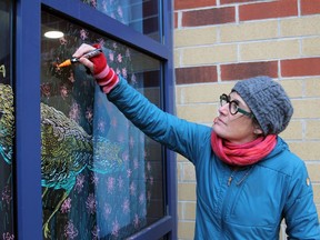 Marney McDiarmid touches up her drawings on the window of Rideaucrest Home's Alzheimer's wing in Kingston on Monday. (Steph Crosier/The Whig-Standard)