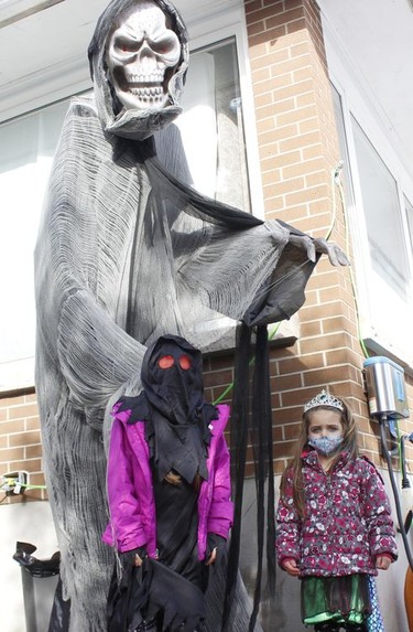 Siblings Khloe Grenier, 8, and Brielle, 3, stand next to one of the displays outside the haunted house tour on Toke Street on Saturday. 

RICHA BHOSALE/The Daily Press