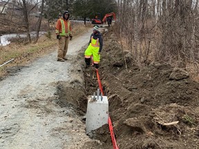 Workers with Raw Electric install concrete bases for lampposts along the side of the Junction Creek trail near Leslie Street on Monday.