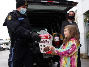 Jamie Lynn Yacks, 6, from Enniskillen Township hands Lambton OPP auxiliary member Malcolm Avery a donation during the OPP's Stuff-a-Cruiser initiative outside the grocery store on Friday December 4, 2020 in Petrolia, Ont. The event, collecting food and toys for local food banks, continues throughout the weekend in Petrolia and Forest. Terry Bridge/Sarnia Observer/Postmedia Network