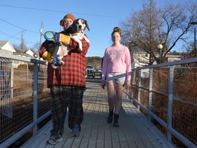 Addam Godfrey, accompanied by Morgan Blacklock, carries Watson the beagle over a pedestrian bridge near the Food Basics on Notre Dame on Wednesday. The dog wasn't too keen on the ridged surface of the span. Jim Moodie/Sudbury Star