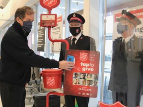 Timmins Mayor George Pirie tries out the new tap-and-go system for donating to The Salvation Army while at Your Independent Grocer on Monday. Next to him is Capt. Robbie Donaldson, regional officer for The Salvation Army in Timmins, while peering through the window and physically distancing is fellow Salvation Army officer Craig Wilson.

ANDREW AUTIO/Local Journalism Initiative