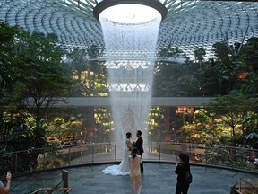 Newlyweds pose for their photographer against the rain vortex at Changi Jewel in Singapore. ROSLAN RAHMAN/AFP via Getty Images)