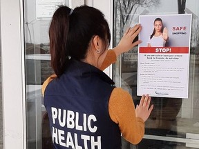 A public health inspector posts a sign at a grocery store warning people recently back from travel to another country not to enter, one of the measures aimed at slowing the spread of COVID-19. (SUBMITTED PHOTO)