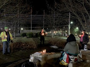 From left, Joe Boisvenue, Brockville Coun. Leigh Bursey and Marcia Church take part in a candlelight vigil to raise awareness of homelessness, at the park behind city hall on Dec. 21, while Jaida Dubois, seated, live-streams the event. Eight people gathered for the second annual event. (RONALD ZAJAC/The Recorder and Times)