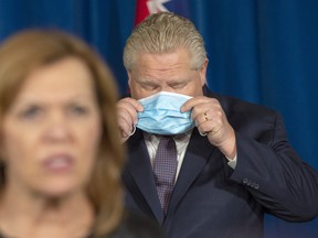 Premier Doug Ford puts his mask back on as Health Minister Christine Elliott speaks at the daily briefing at Queen’s Park in Toronto on Friday, Jan. 8.