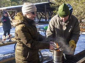 While Kristen Webb tries to attract some chickadees to her handful of seeds, her sister Stefanie Webb and dad Don Webb of Caledon try to toast some hotdog buns to go with their wieners for lunch in Pinery Provincial Park. Mike Hensen/Postmedia Network