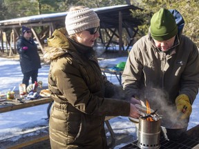 While Kristen Webb tries to attract some chickadees to her handful of seeds, her sister Stefanie Webb and dad Don Webb of Caledon try to toast some hotdog buns to go with their wieners for lunch in Pinery Provincial Park. (Mike Hensen/The London Free Press)
