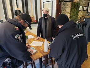 Only minutes after opening his Front Street premises Wednesday, Kyle Thomson, centre, owner-proprietor of Park Provisioners Barbershop & Haberdashery, was fined by Belleville Police and issued a public health order warning by Roberto Almeida, program manager, right, with Hastings-Prince Edward Public Health. DEREK BALDWIN