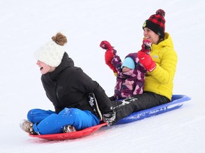 Chelsea Sterling, left, three-year-old Adeline Depuydt and Alex Depuydt toboggan down the hill at Kingston Park in Chatham on Feb. 19. Mark Malone/Postmedia Network