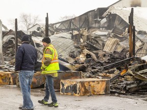 Randy Loewen, right, talks to another firefighter Thursday as they walk past debris from a fire that broke out Wednesday evening at Walker Dairy Farm near Aylmer. About 100 cows were killed in the blaze and damage is estimated at $5 million.