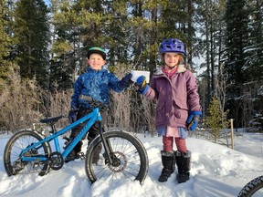 Jack Deoliveira and Bella Bullock hand over the cheque donation to Canmore and Area Mountain Bike Association (CAMBA) on Feb. 5 at Quarry Lake, Canmore. The trail that both children stand in front of doesn't have an official name yet. It's a short connector trail that has been very popular with the younger riders, and a lot of the children call it the "Fun Forest". Photo submitted.