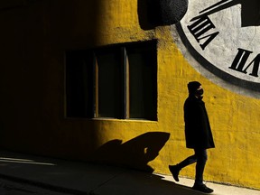 A man wearing a protective mask walks into the sunlight on a cold afternoon during the COVID-19 pandemic. PHOTO BY NATHAN DENETTE /THE CANADIAN PRESS