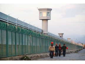 Workers walk by the perimeter fence of what is officially called a 'vocational skills education centre' in Dabancheng in Xinjiang Uyghur Autonomous Region. Repression of Muslim minorities by the Beijing government has been called genocide by international law experts.