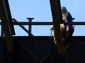 A welder is illuminated by his torch as he welds supports onto the main beams of a building. (Mike Hensen/The London Free Press)