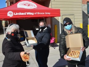 United Way of Bruce Grey Executive Director Francesca Dobbyn, left, holds up the specially designed Pi Day medallion, while OSHaRE Executive Director Colleen Trask Seaman and Teresa Pearson, a manager at Canadian Mental Health Association Grey Bruce hold up pies outside the Owen Sound Hunger and Relief Effort facilities in downtown Owen Sound on Saturday, March 13, 2021.
