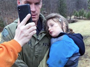 Ontario Provincial Police Const. Scott McNames carries Jude Leyton, 3, back to his family in South Frontenac while FaceTiming his parents on Wednesday. Jude had been missing in the thick forest for three and a half days.