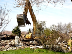The backhoe that tore down a Shakespeare home following an early morning fire Monday helps firefighters sift through the charred rubble shortly before noon. Galen Simmons/The Beacon Herald/Postmedia Network