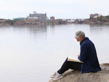 Joanne Proulx sits on a rock while journaling at Ramsey Lake in Sudbury, Ont. on Thursday April 29, 2021. Sudbury has garnered a reputation around the world as a community that knows how to recover an environment degraded by mining and smelting operations. Most of that know-how was developed by Laurentian University researchers -- expertise that will be lost as the university restructures, critics warn. John Lappa/Sudbury Star/Postmedia Network