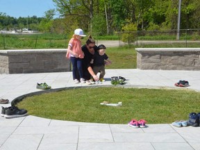 Rebecca Brown and her children Cora, 5, and Eddie, 1, place shoes at the Giche Namewikwedong Reconciliation Garden at Kelso Beach on Monday to honour the 215 children whose bodies were found buried at a residential school in Kamloops, B.C.