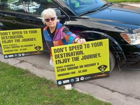 Francesca Dobbyn, secretary of the Bruce Peninsula Safe Communities committee and executive director of the United Way of Bruce Grey, poses with two of the signs the committee made available to landowners on Highway 6 between Wiarton and Tobermory in an effort to curb stunt and erratic driving on the peninsula.  SUPPLIED