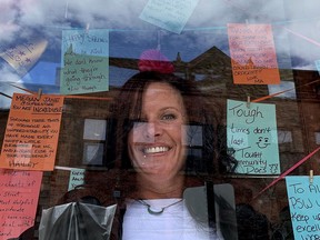 Laura Phipps poses with some of the messages of kindness posted in the storefront at Heather & Crow downtown, amid the reflection of the sky and King Street, on Thursday afternoon. (RONALD ZAJAC/The Recorder and Times)