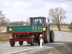 A tractor with a trailer rides on an asphalt road, with a slightly faded slow moving sign.
Not Released