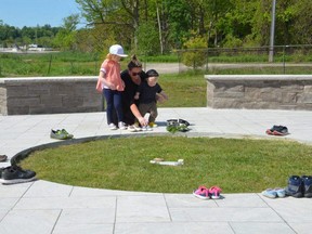 Rebecca Brown and her children Cora, 5, and Eddie, 1, place shoes at the Giche Namewikwedong Reconciliation Garden at Kelso Beach on Monday to honour the 215 children whose bodies were found buried at a residential school in Kamloops, B.C.